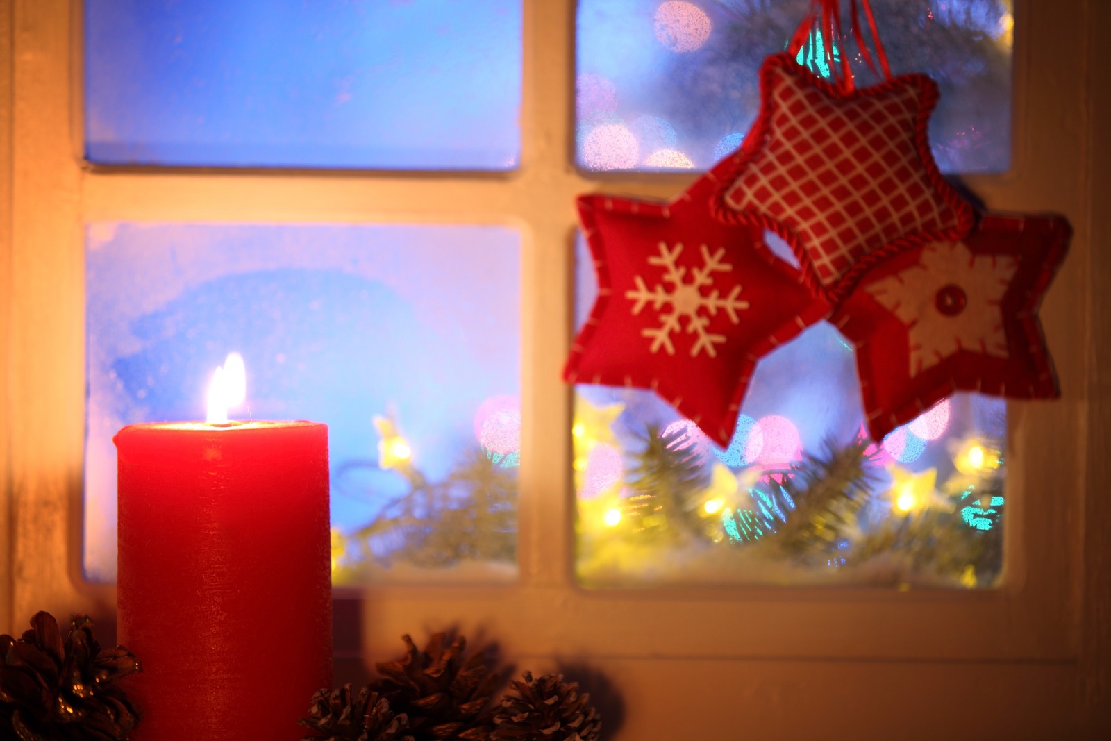 Las velas están encendidas frente a una ventana con decoración navideña (día de navidad, decoración navideña, festivo, luces navideñas, ventana de navidad)