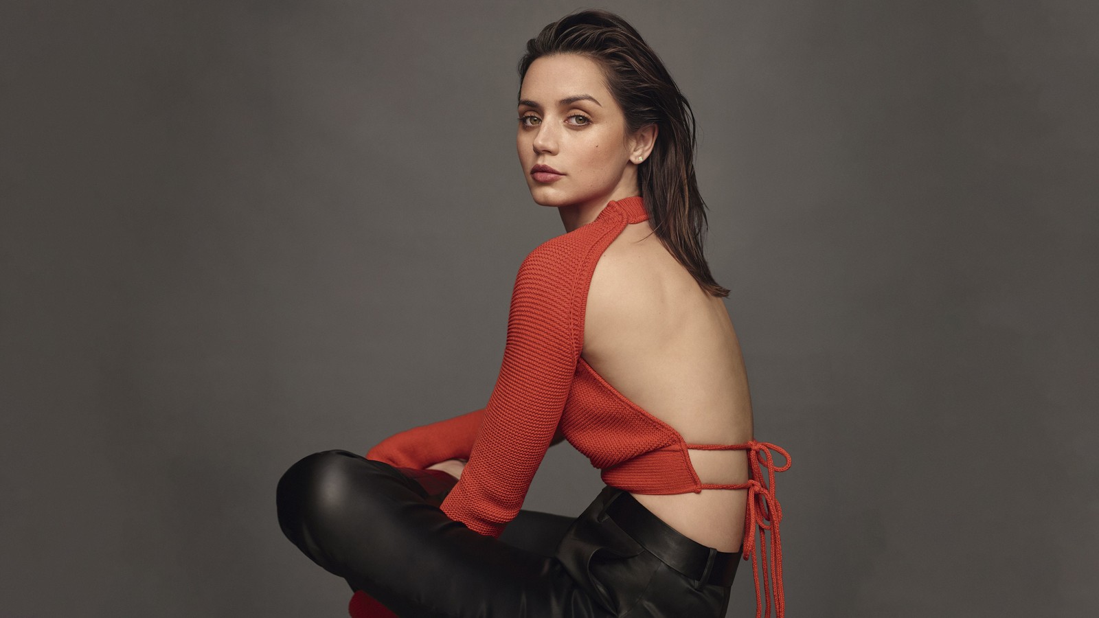 Una mujer con un suéter rojo y pantalones negros sentada en un taburete (ana de armas, moda, 2023, gente, fondo de pantalla 4k)