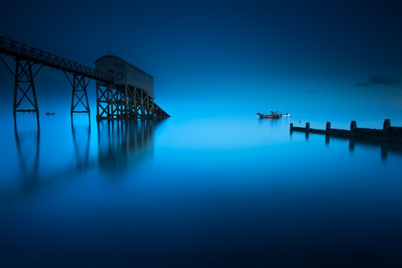 Пирс с лодкой вдали и голубым небом (selsey lifeboat station, англия, england, морской пейзаж, синий фон)