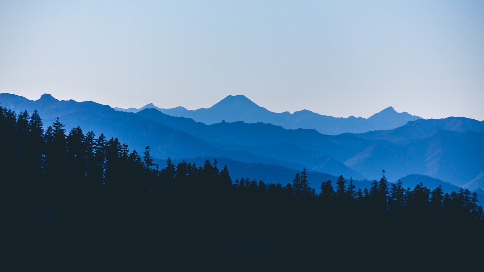 Uma vista de uma cordilheira com algumas árvores em primeiro plano (montanhas, paisagem, floresta, cenário)