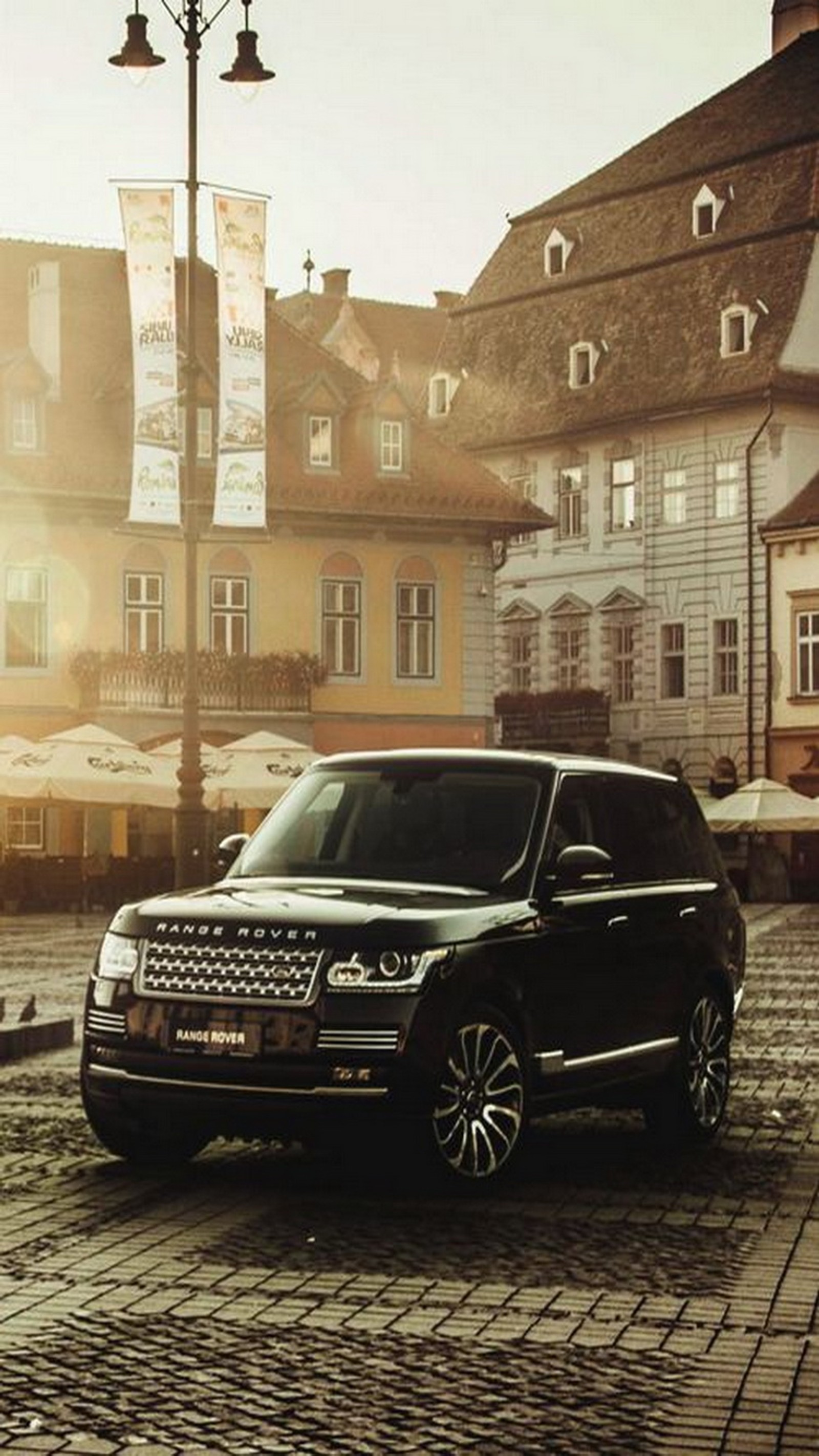 A close up of a black range rover parked on a cobblestone street (italy, range rover)