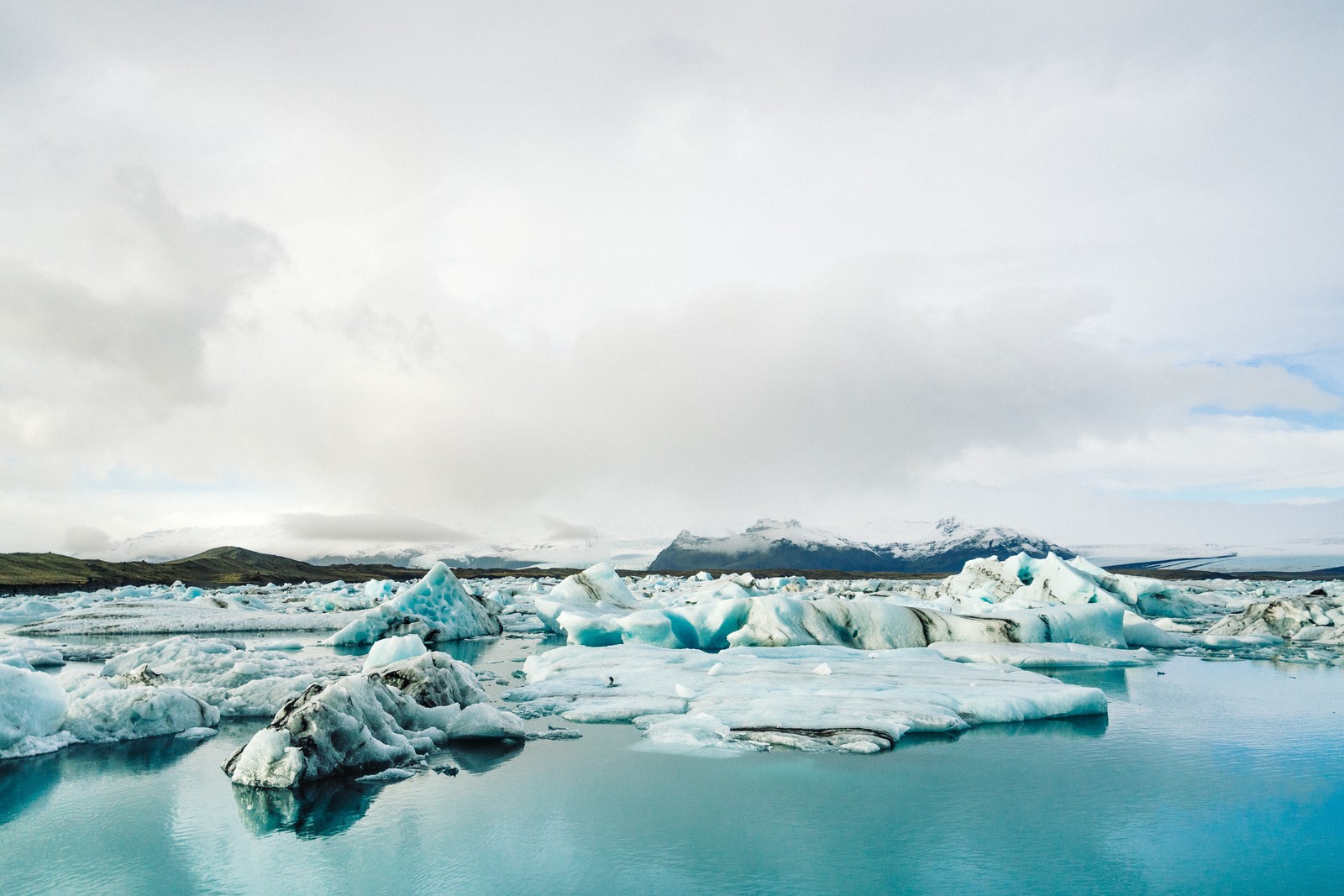 Icebergs árabes flutuando en un lago con una montaña al fondo (glaciar, cueva glaciar, fiordo, iceberg, nube)