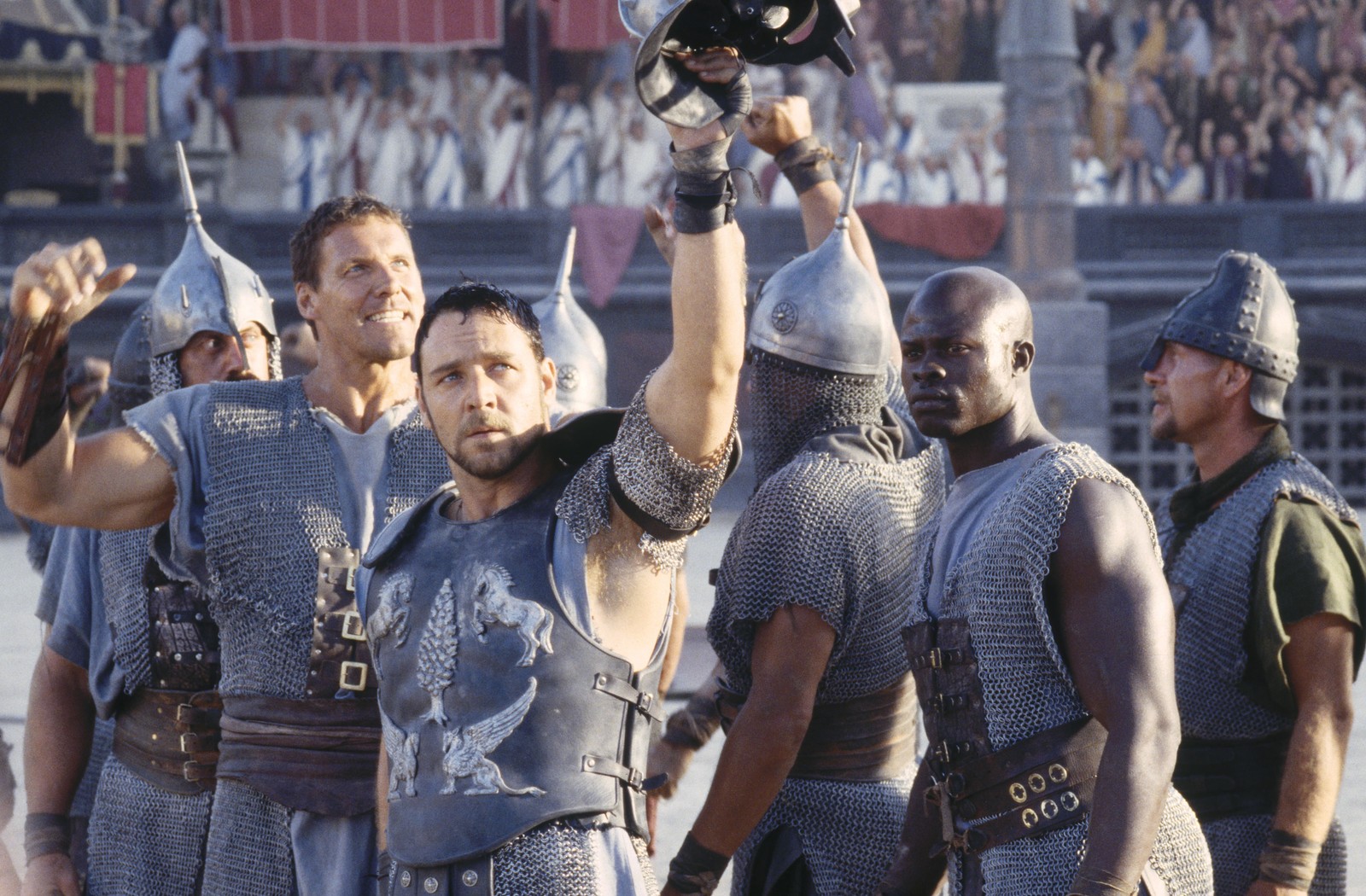 Gruppe von männern in rüstung, die einen helm in einem stadion hochhalten (russell crowe, gladiator, menge, kolosseum, film)