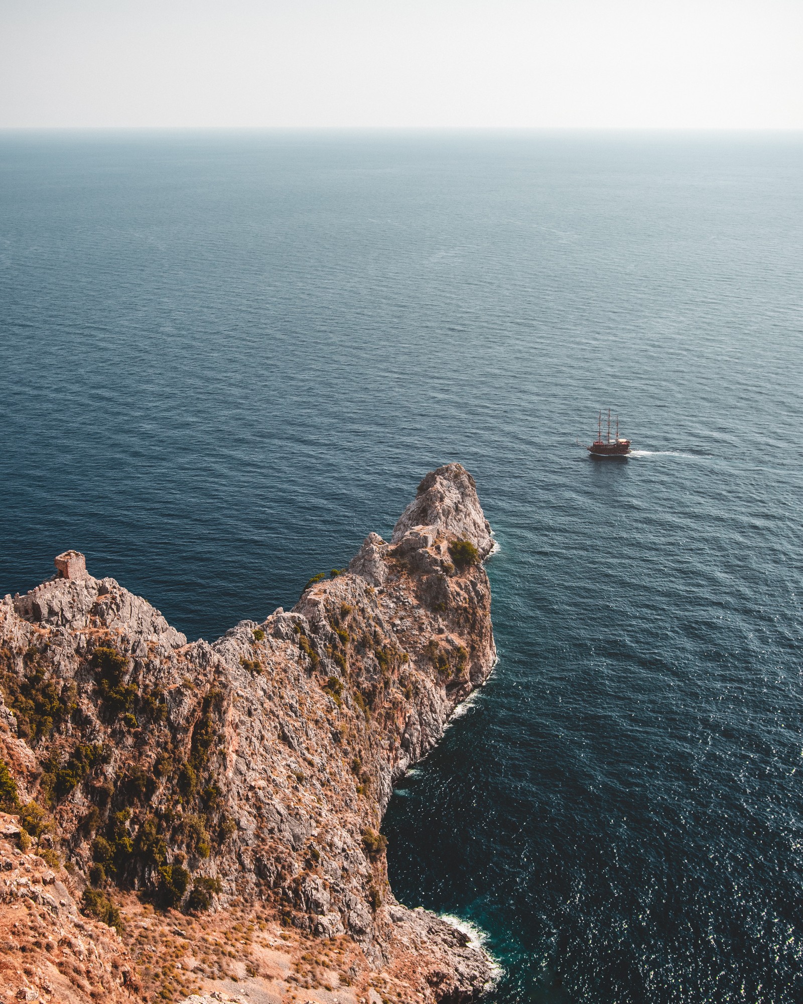 Há um barco navegando na água perto de um penhasco (mar, costa, penhasco, klippe, promontório)