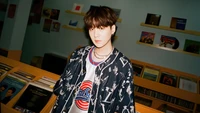 Min Yoon-gi (Suga) dans une tenue élégante, debout dans un magasin de musique vibrant entouré de disques vinyles.