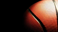 Close-up of a basketball against a black background, highlighting its textured surface and vibrant color.