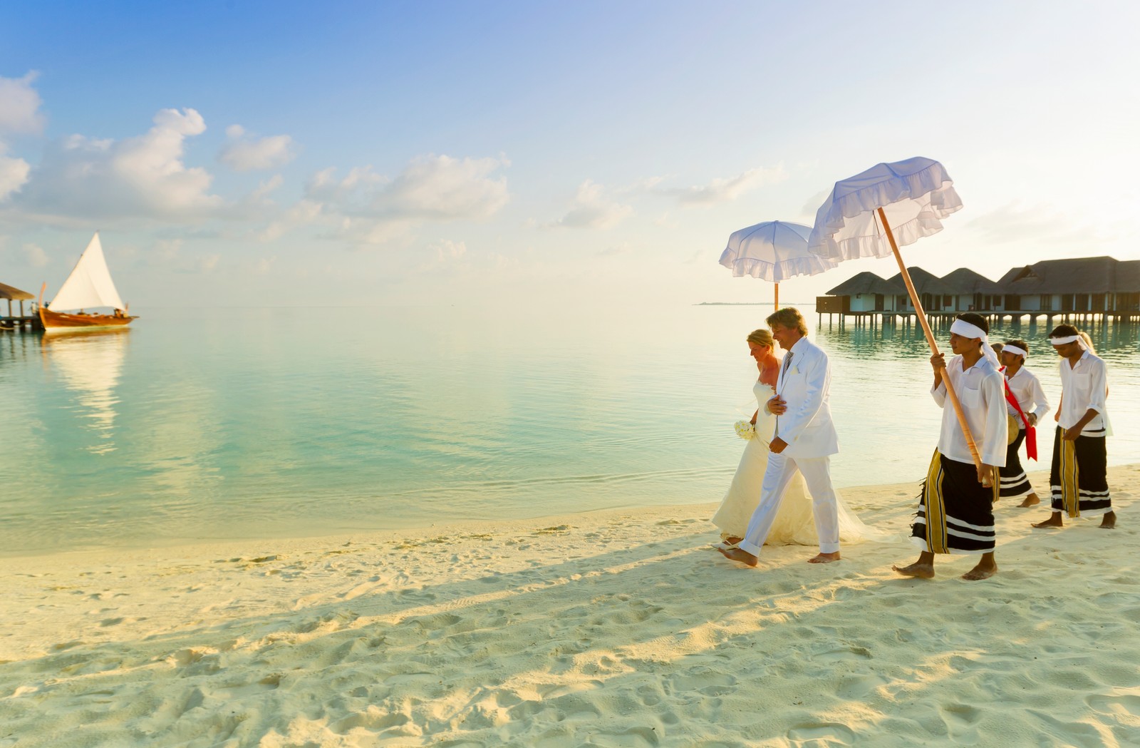 Plusieurs personnes marchant sur une plage avec des parasols dans le sable (velassaru maldives, vacances, lune de miel, tourisme, plage)