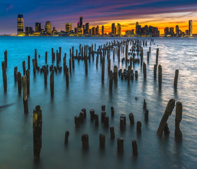 Вид на силуэт города с воды на закате (старые пирсовые столбы, нью йорк, new york city, горизонт, городской пейзаж)