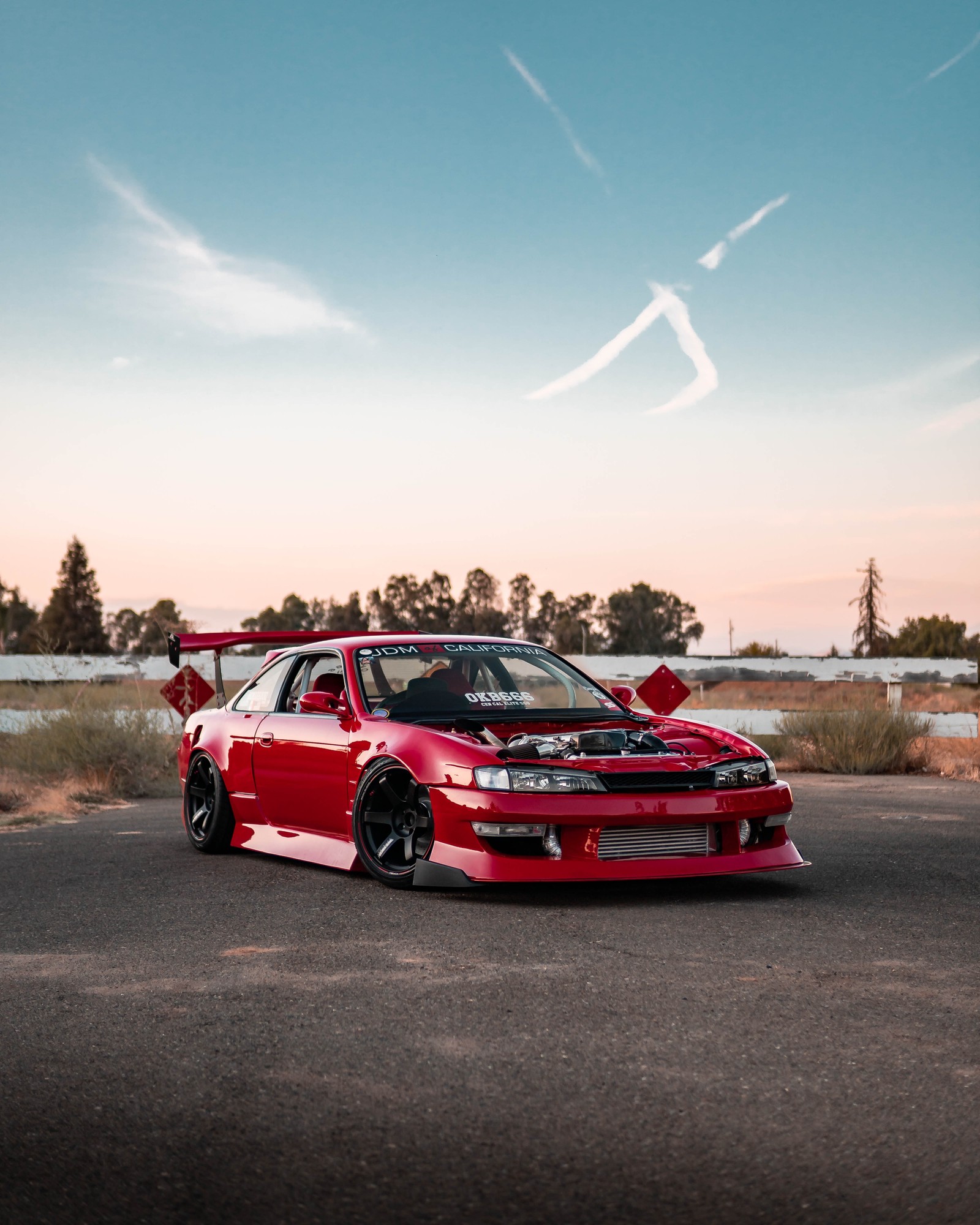 A close up of a red car parked on a road near a fence (sports car, red, drifting, king, sky)