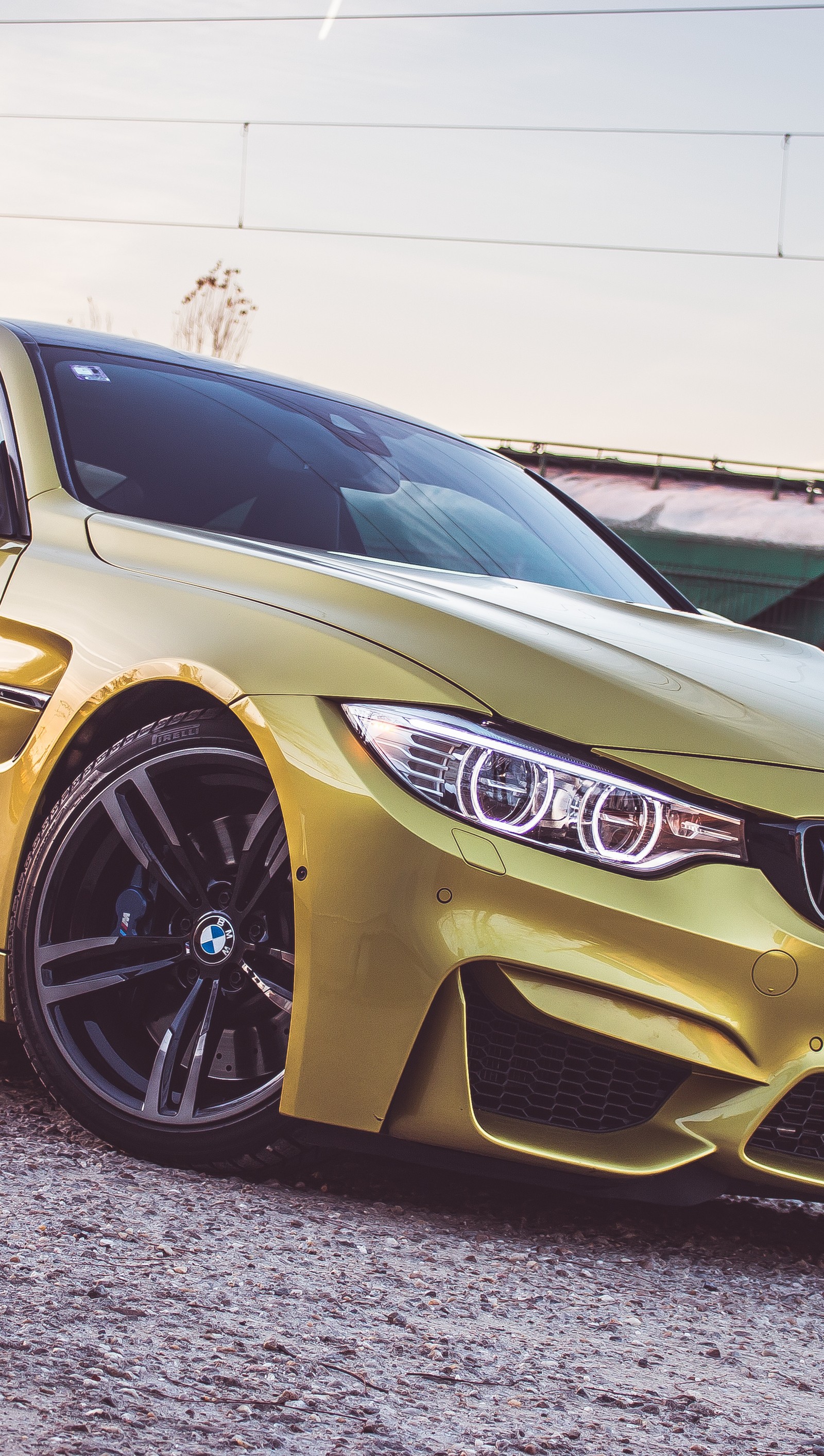 Un primer plano de un coche bmw amarillo estacionado en un camino de grava (angeleyes, bmw, m4, mperformance, fotografía)