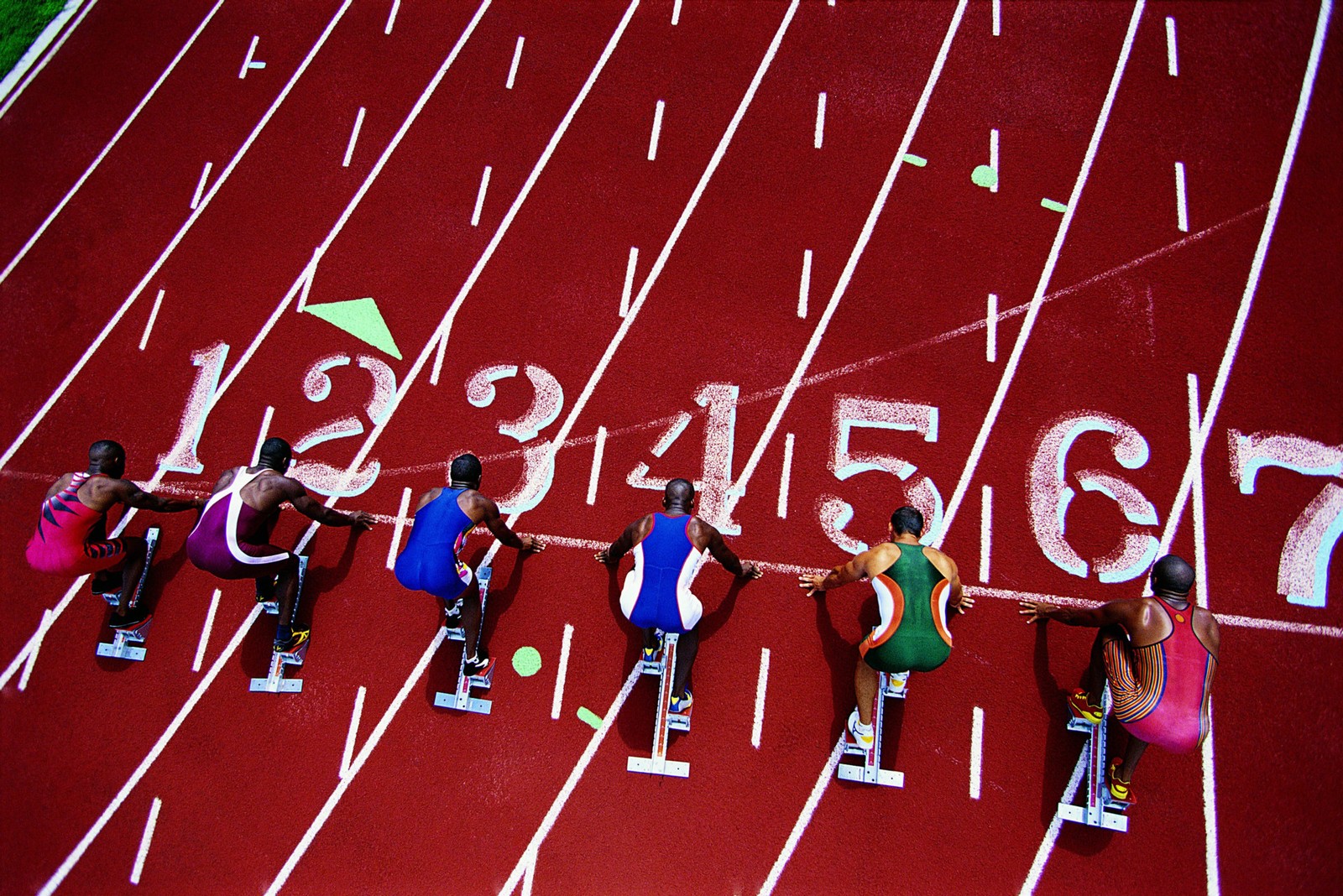 Várias pessoas sentadas em uma pista com a palavra 'equipe' pintada nela (atletismo, estádio, esportes, decathlon, local desportivo)