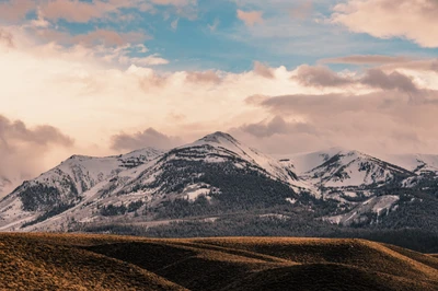 Des montagnes enneigées s'élèvent majestueusement contre un fond de nuages doux, mettant en valeur la beauté sauvage de la nature dans un paysage naturel serein.