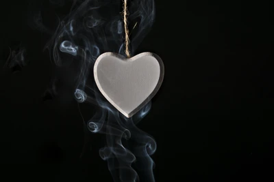 Pendentif en forme de cœur blanc entouré de fumée sur un fond sombre