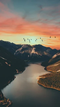 Coucher de soleil majestueux sur un lac serein avec des oiseaux en vol et des montagnes de haute altitude