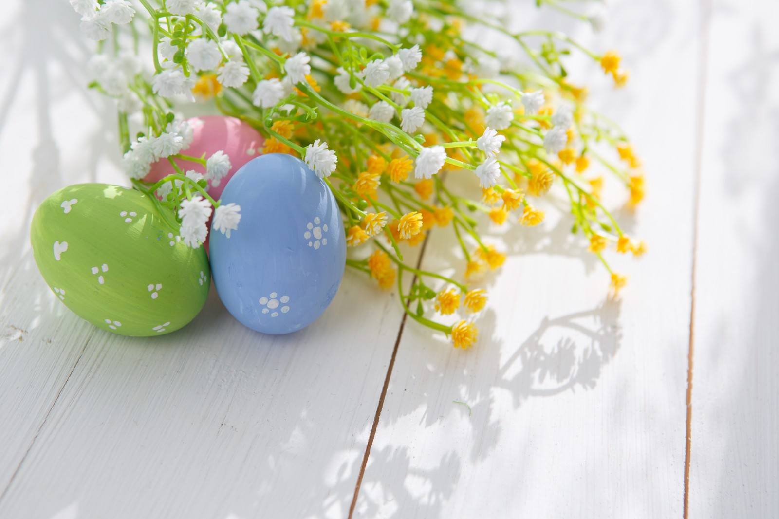 Hay tres huevos y flores sobre una mesa blanca (huevo de pascua, pascua)