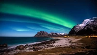 Faszinierende Aurora Borealis über den schneebedeckten Bergen und der felsigen Küste der Lofoteninseln