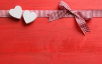 Red background featuring two white wooden hearts and a red and white checked ribbon bow.