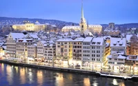 Paisagem urbana coberta de neve em Zurique ao anoitecer, exibindo arquitetura histórica e reflexos no rio.