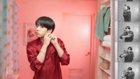 Jungkook em um banheiro, se preparando com uma expressão brincalhona, capturado em tons vibrantes de rosa.