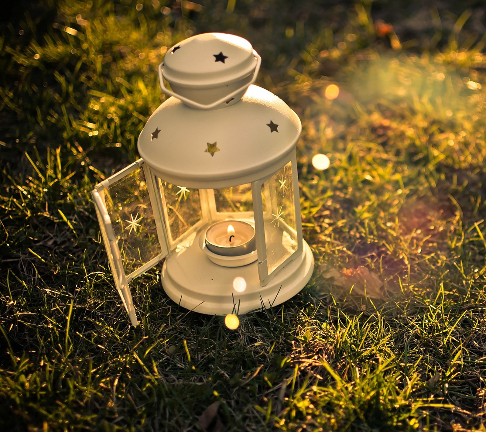 There is a white lantern sitting on the grass with a candle (hd, lantern)