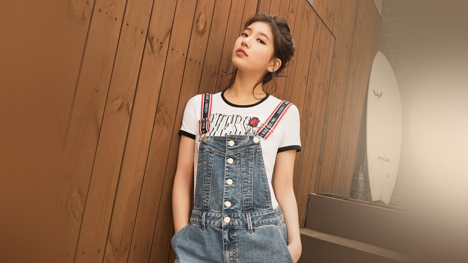 Une femme arabe en chemise blanche et salopette en denim s'appuyant contre un mur en bois (suzy, 배수지, actrice, kpop, k pop)