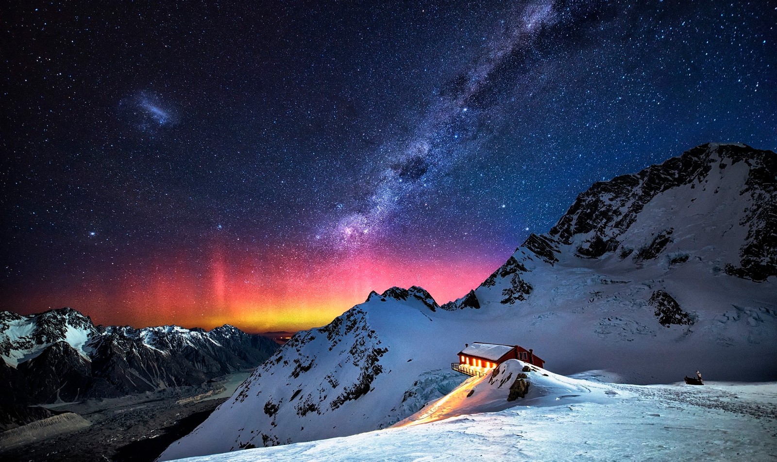 Uma vista de uma cabana em uma montanha nevada com um céu auroral brilhante (via láctea, inverno, montanha, aurora, neve)