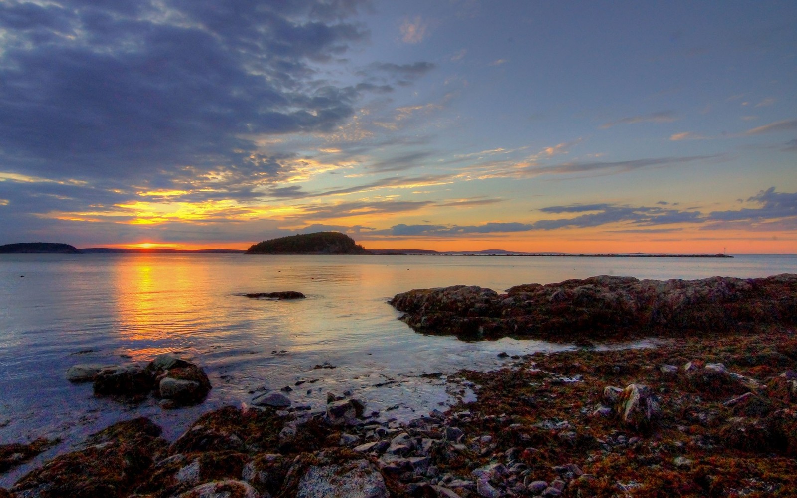 A view of a sunset over a body of water with rocks and a small island in the distance (sunset, sea, horizon, coast, shore)