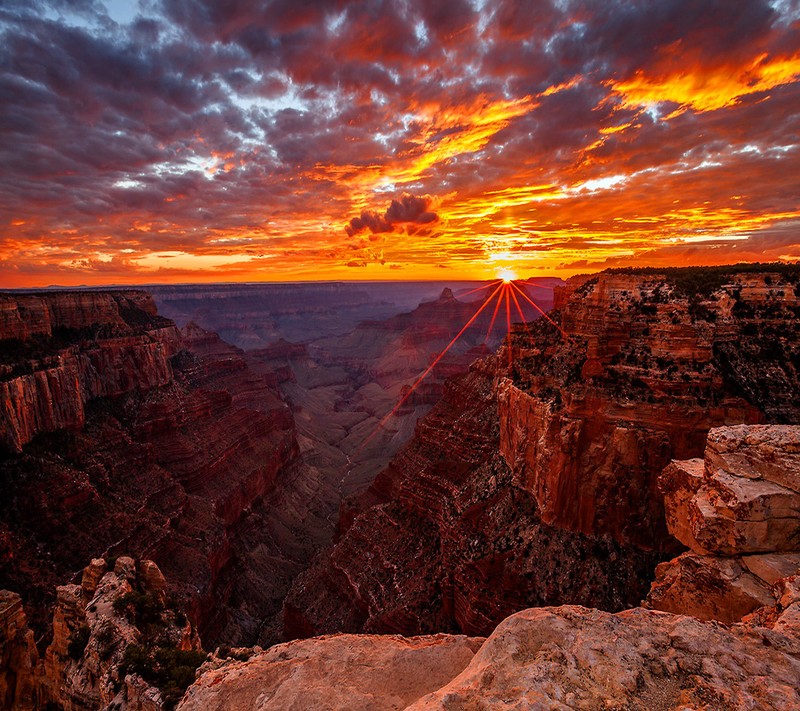 Une vue d'un coucher de soleil sur un canyon avec un ciel orange vif (paysage, papier peint)