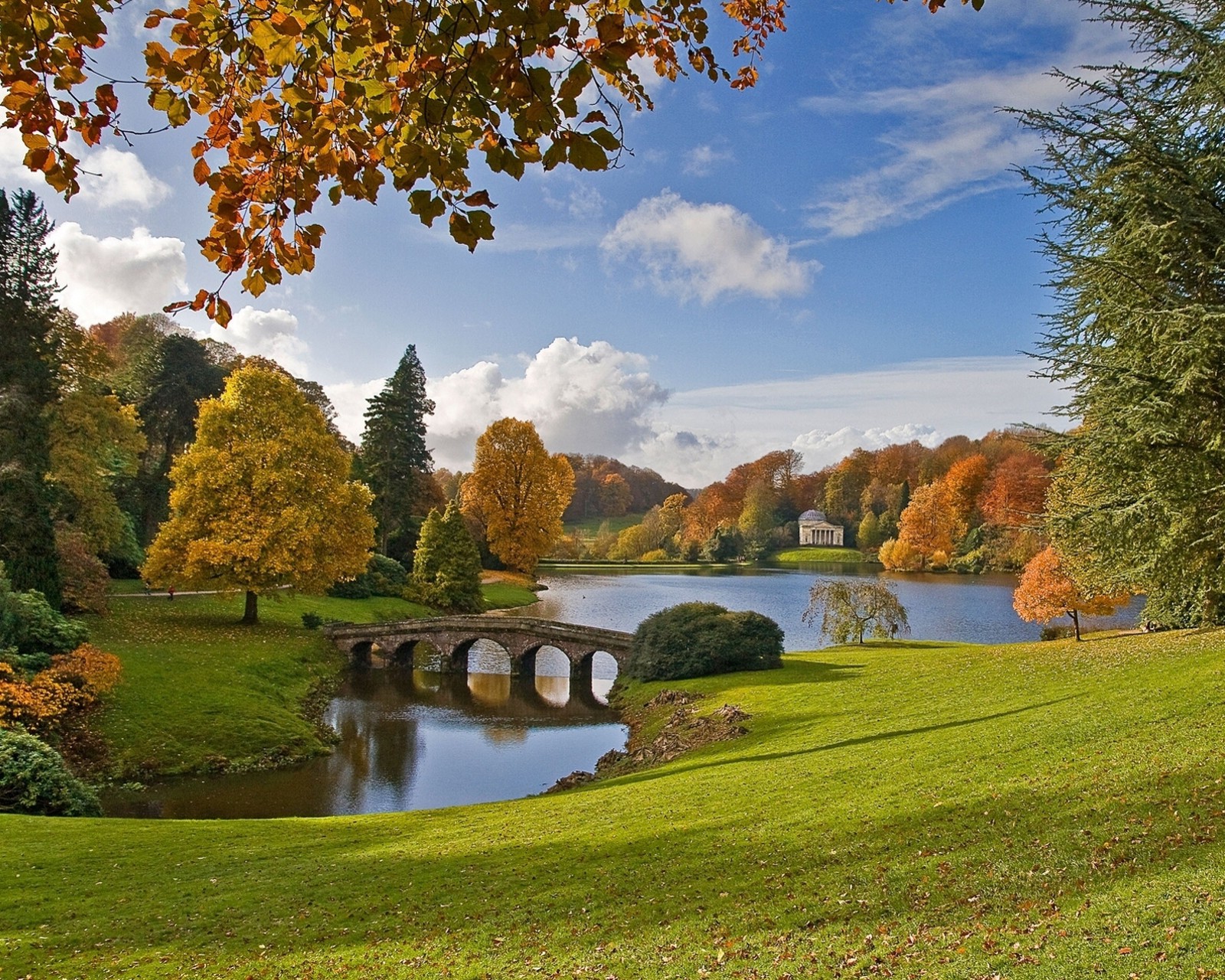 Des arbres au premier plan et un pont au-dessus d'un lac (automne, pont, angleterre, england, lac)