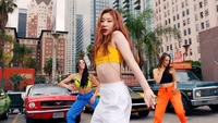 Chaeryeong from ITZY performing with vibrant energy against a backdrop of urban architecture and classic cars.