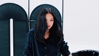 Jennie von BLACKPINK strahlt Selbstbewusstsein und Stil in einem eleganten schwarzen Outfit vor einem minimalistischen Hintergrund aus.