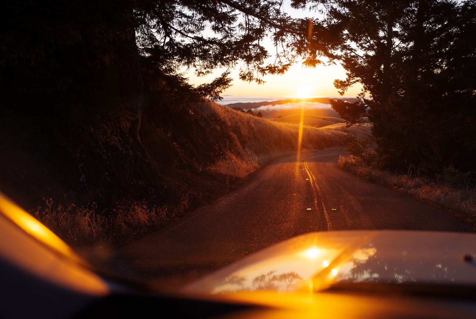 Vue d'une voiture roulant sur une route en terre au coucher du soleil (coucher de soleil, ensoleillement, lumière, route, chaleur)