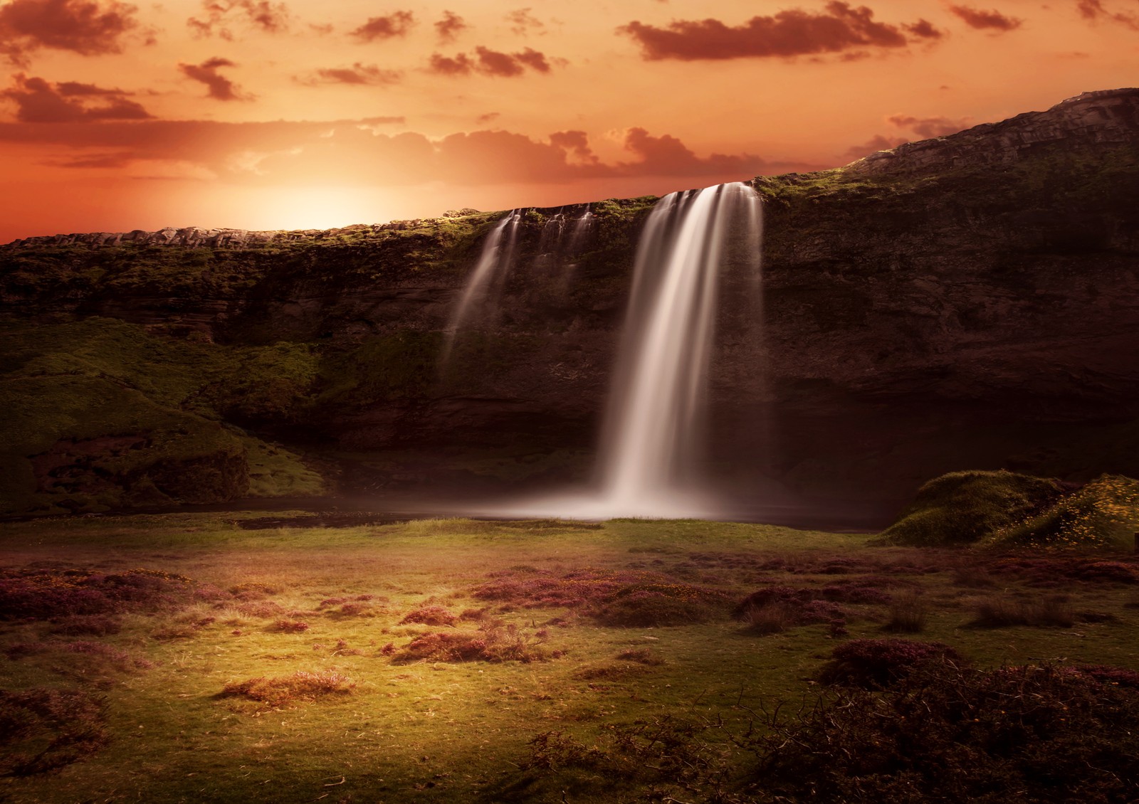 A close up of a waterfall with a sunset in the background (waterfalls, sunrise, orange sky, clouds, grass landscape)