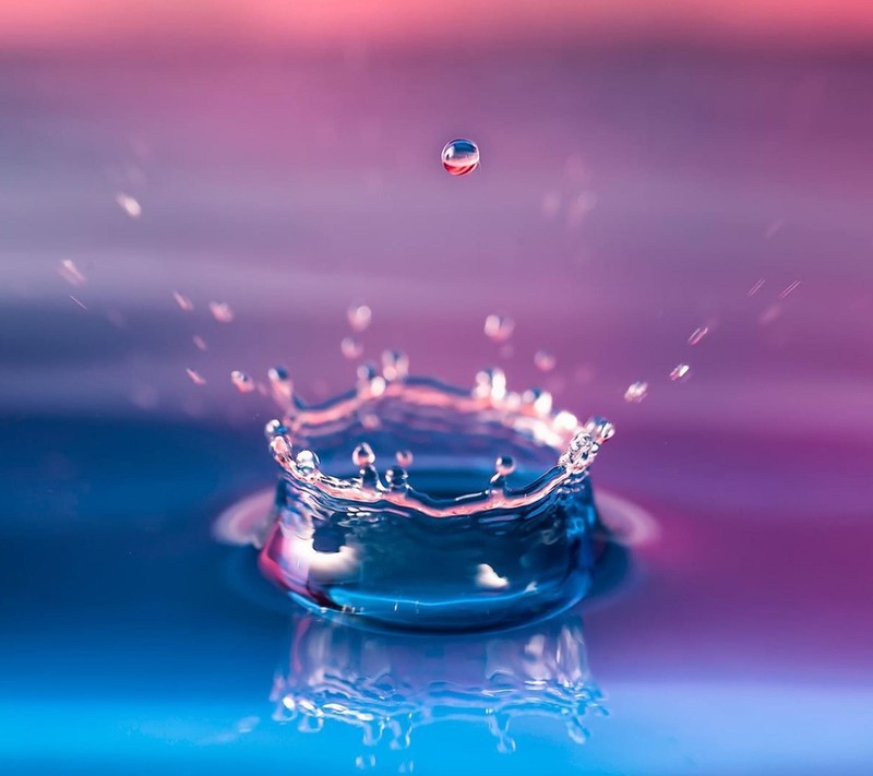 Un gros plan d'une goutte d'eau sur un fond rose (bleu, eau)