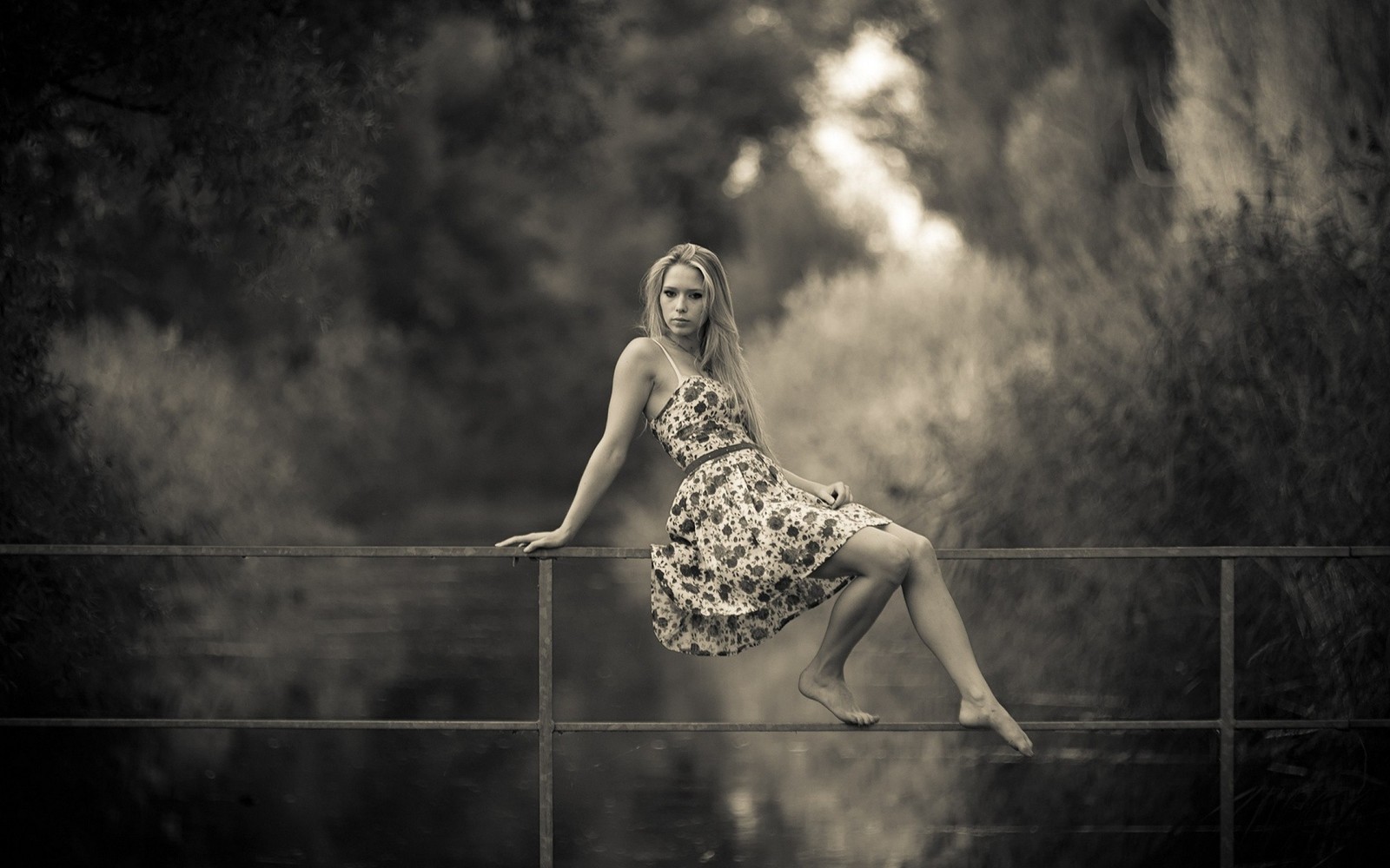 Arafed woman sitting on a fence in a dress by a river (black and white, monochrome, beauty, blond, monochrome photography)