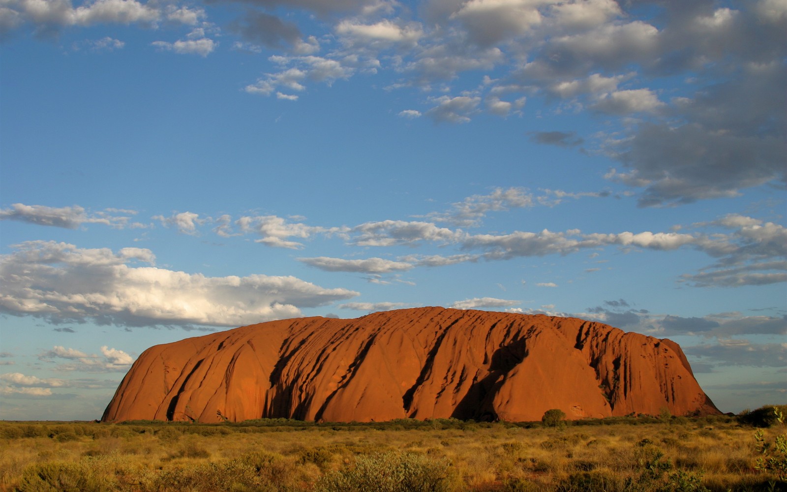 Roca árabe en medio de una llanura de hierba bajo un cielo nublado (uluru, interior de australia, badlands, nube, roca)