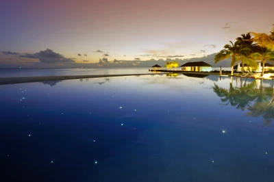 Ruhiges Strandresort bei Sonnenaufgang, mit einem ruhigen Infinity-Pool, der den klaren Himmel und den Horizont widerspiegelt.