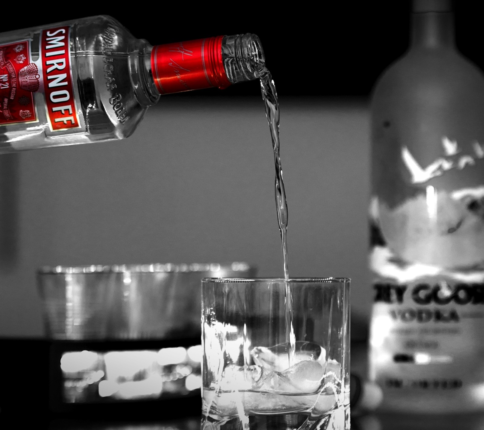 Someone pouring vodka into a glass with ice cubes in it (ice, red, smirnoff)