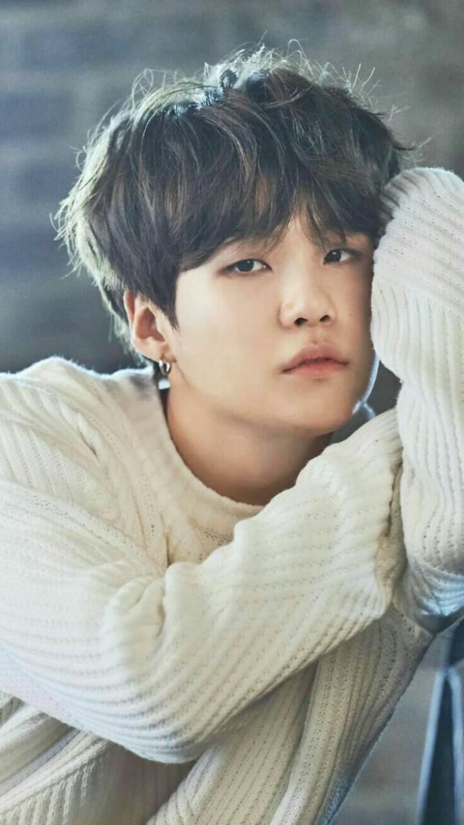 Un gros plan d'une personne s'appuyant sur une chaise avec un pull (bts, suga)