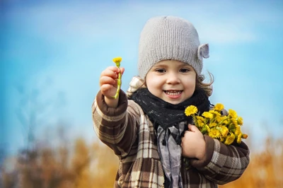 Fröhliches Mädchen mit Strickmütze, das Blumen hält