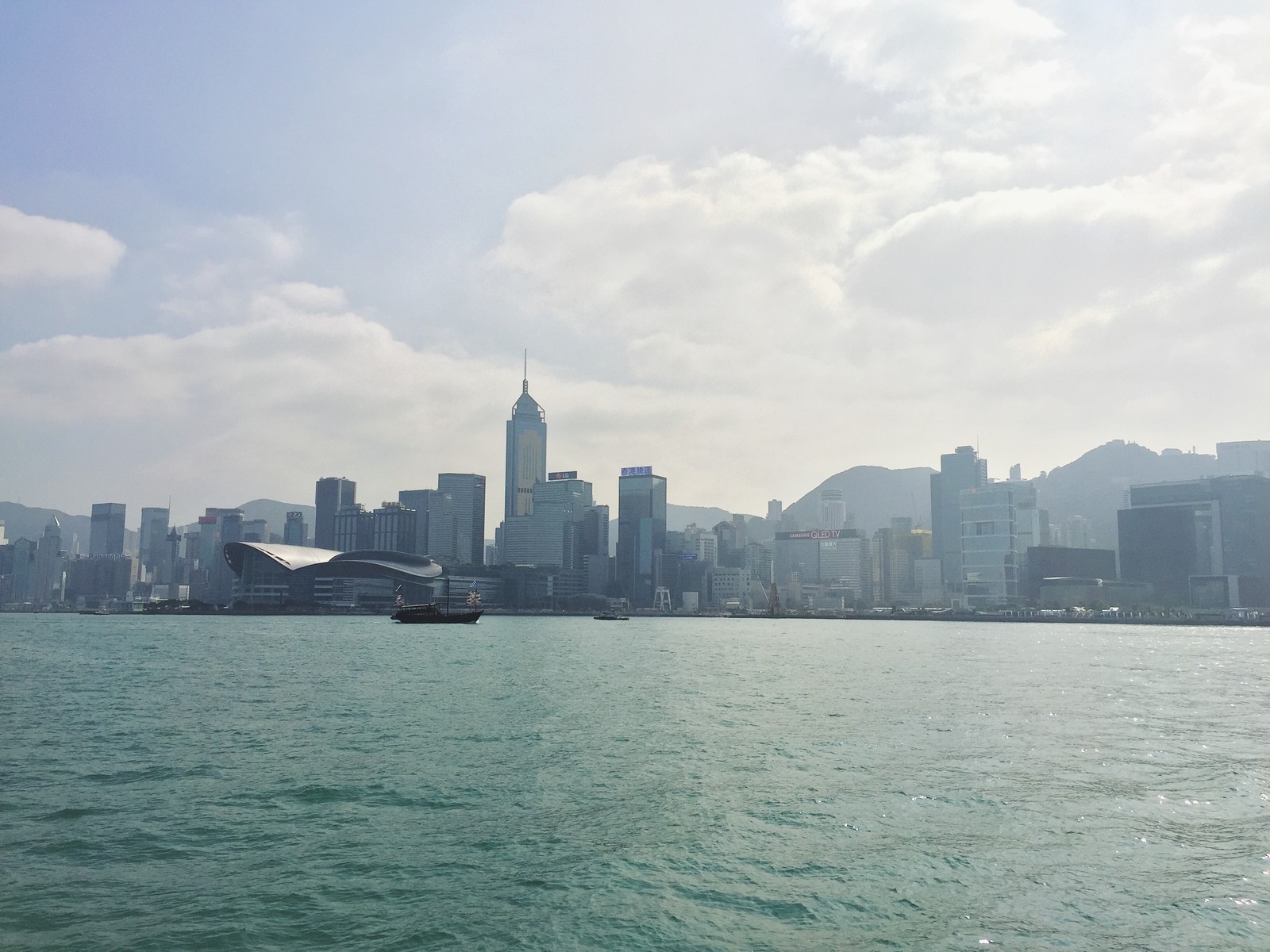 Um barco na água com uma cidade ao fundo (hong kong, linha do horizonte, água, mar, arranha céus)