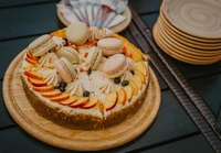 Delicious cheesecake adorned with fresh fruit, macarons, and cream swirls, served on a rustic wooden platter.