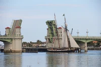 Sailing ship passing under a raised bridge on a calm waterway.