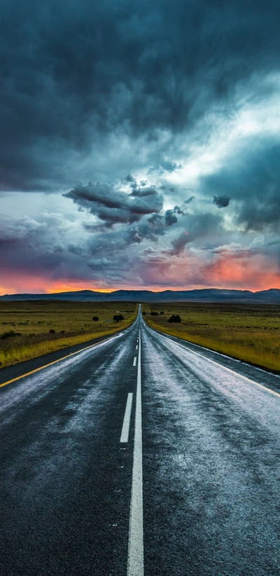 Route droite à travers un paysage nuageux au crépuscule