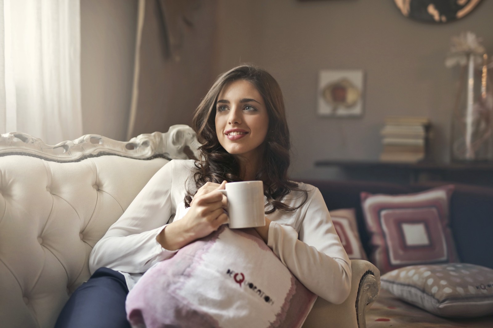 Mujer sentada en un sofá sosteniendo una taza de café (sentado, retrato, sonrisa, habitación, almohada)