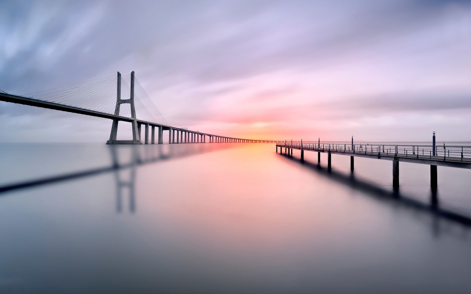 Uma vista de uma ponte que está sobre um corpo d'água (ponte, água, cais, horizonte, reflexo)