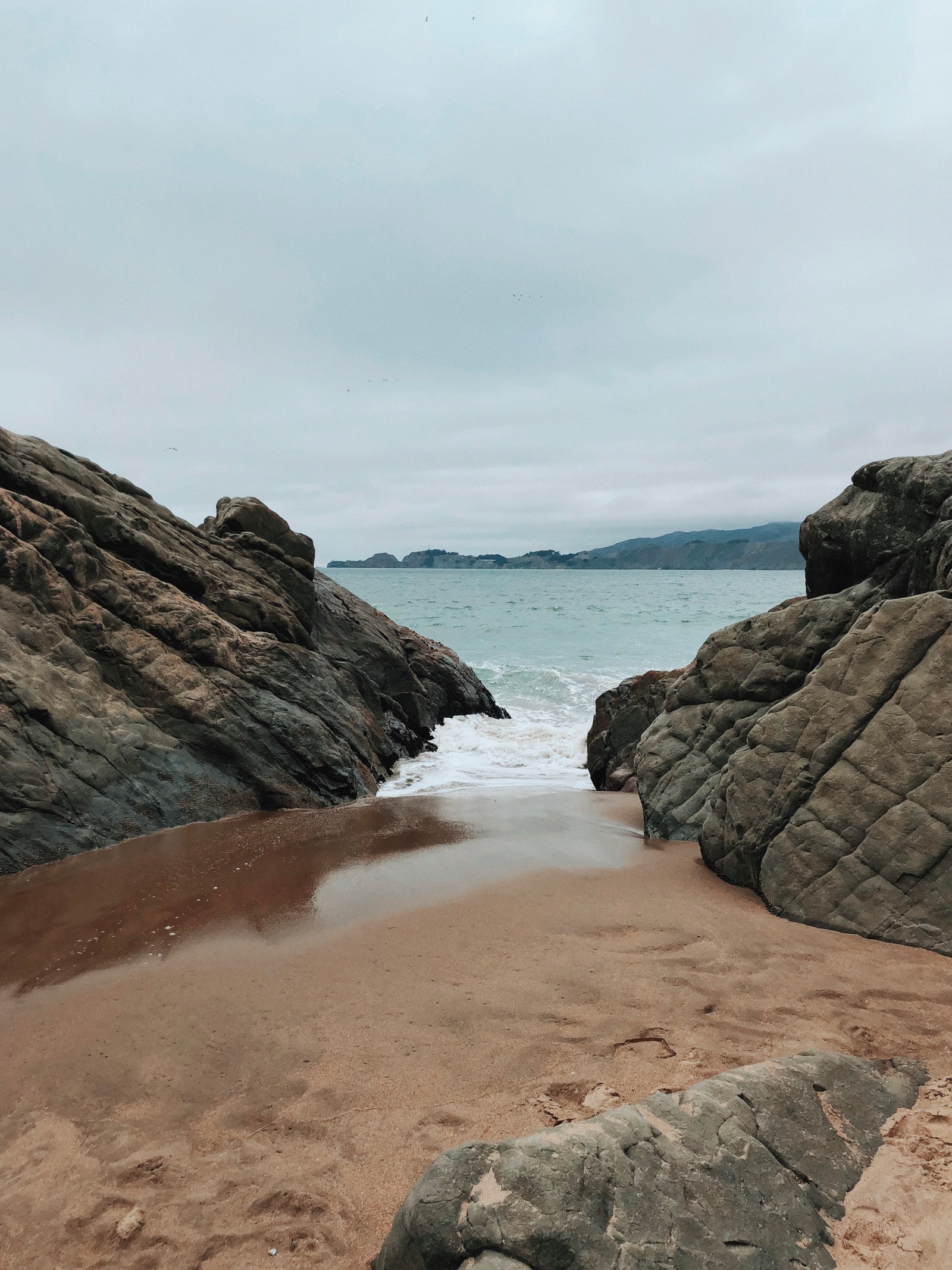 There is a sandy beach with a few rocks and water (sea, rock, water resources, bedrock, watercourse)