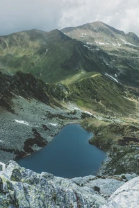 Un sereno lago de cráter enclavado entre montañas de tierras altas, rodeado de terreno rocoso y exuberante vegetación.