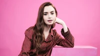 Lily Collins en un atuendo de patrón elegante contra un vibrante fondo rosa.