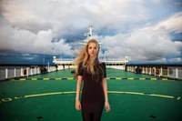 Blonde Model in einem schwarzen Kleid vor einem dramatischen Himmel während eines malerischen maritimen Urlaubs